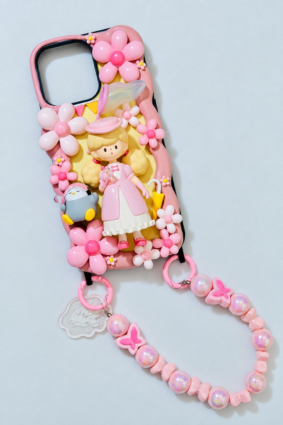 Decoden-Handyhülle mit rosa Cremeblumen, Puppenfigur, Pinguin-Anhänger und rosa Perlenkette
